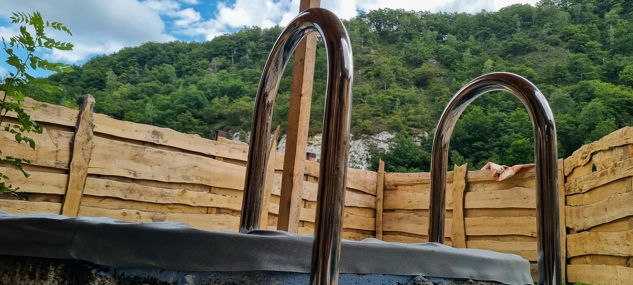 Купель под открытым небом и лесной склон за оградой